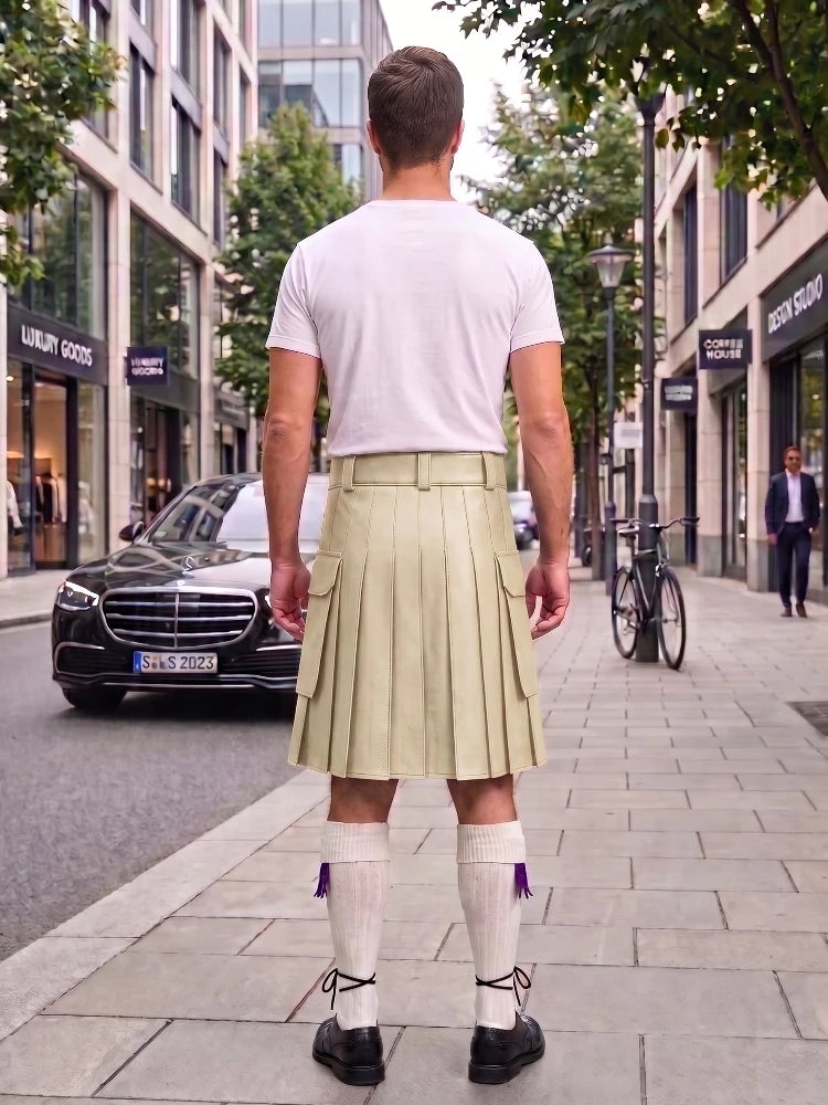 A man viewed from behind wearing a white t-shirt and a light beige pleated kilt with white knee-high socks, standing on a city sidewalk.