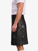 A man wearing a black faux-leather kilt with pleated detailing and gold-tone button accents, paired with a white t-shirt, shown from the side against a light gray background.