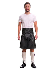 A man modeling a black faux-leather kilt with a matching black waist belt and pouch, paired with a white t-shirt, cream knee-high socks, and black lace-up shoes, against a plain white background.