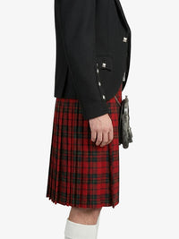 Person wearing a black blazer and red plaid kilt on a white background