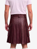 A person shown from the back wearing a pleated dark burgundy leather kilt with side flap pockets, paired with a light pink t-shirt and white socks, against a plain light gray background.