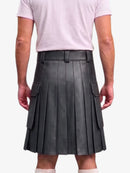 A person shown from the back wearing a dark gray pleated leather kilt with side cargo pockets, paired with a light pink t-shirt and white socks, against a plain light gray background.