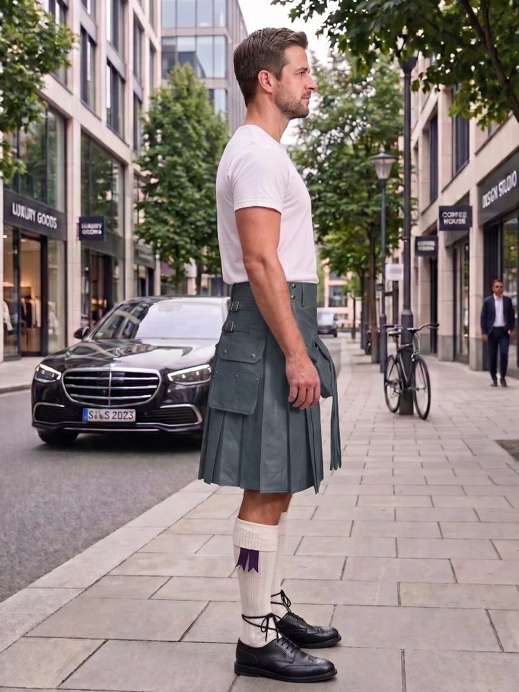 A man standing on a city sidewalk wearing a white short-sleeve t-shirt, a dark gray leather kilt, white knee-high socks with a purple accent, and black leather shoes. A black Mercedes-Benz car and a bicycle are parked on the street behind him.