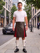 A man stands on a city sidewalk wearing a white crew-neck t-shirt and a dark brown leather kilt with red side panels, paired with white knee-high socks and black leather shoes.