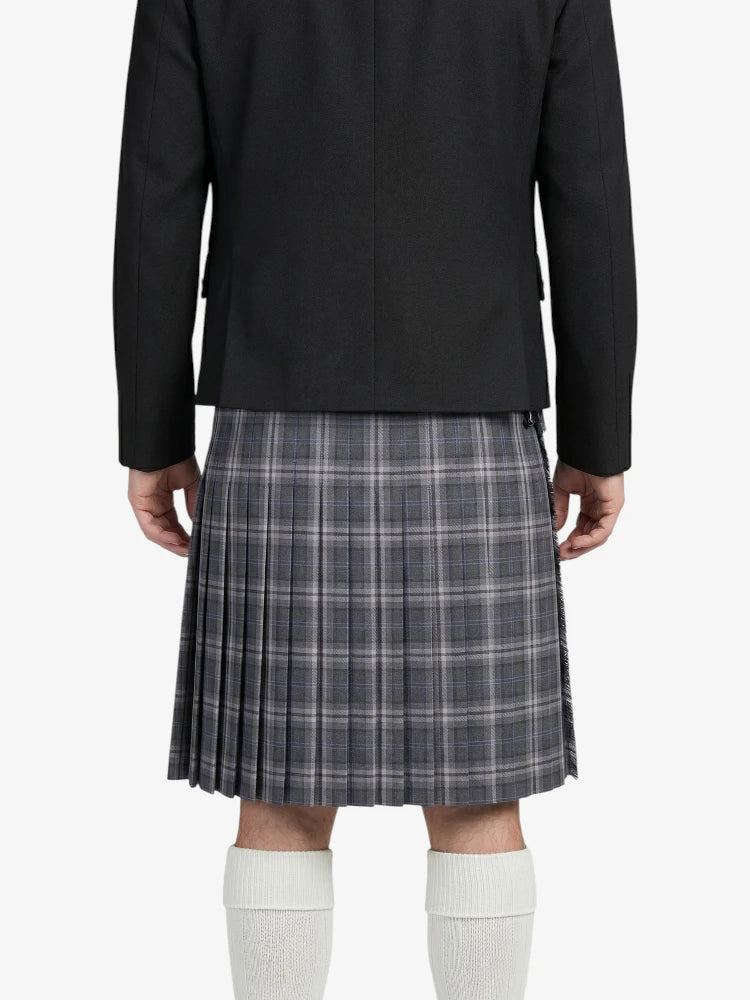 Person wearing a black blazer and plaid kilt on a white background