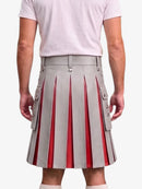 A person shown from the back wearing a light gray pleated kilt with vertical red pleated inserts and side flap pockets with metal snap details, paired with a pale pink T-shirt and white socks against a light gray studio background.
