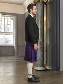 Man wearing a dark jacket, purple kilt, white socks, and black shoes in an elegant interior setting.