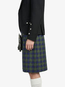 Person wearing a black jacket and green plaid kilt on a white background