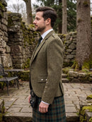 A man in profile wearing a brown tweed blazer and a green tartan kilt, standing outdoors in a stone garden setting.