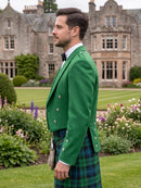 A man in profile wearing a bright green Scottish blazer and a green tartan kilt, standing in a lush garden with a large stone mansion in the background.