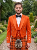 A man wearing a bright orange Scottish formal jacket and matching kilt with a black bow tie and sporran, standing in a garden setting.