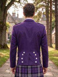 A man viewed from behind wearing a purple Scottish kilt jacket with silver buttons and a purple plaid kilt, standing on a stone path in front of a large stone castle.