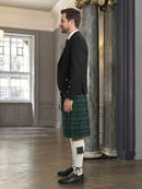 Man wearing a black jacket and green plaid kilt in an elegant interior setting.