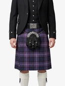 Person wearing a black jacket, purple plaid kilt, and white knee-high socks on a white background