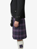Person wearing a black jacket and purple plaid kilt on a white background