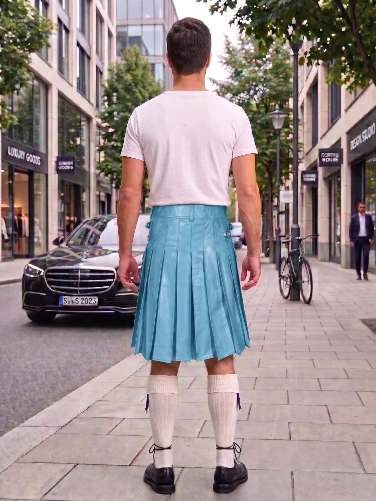 A man standing on a city sidewalk, viewed from behind, wearing a white t-shirt, a bright turquoise pleated leather kilt, white knee-high socks, and black leather shoes. Storefronts, trees, and a parked black Mercedes are visible in the background.