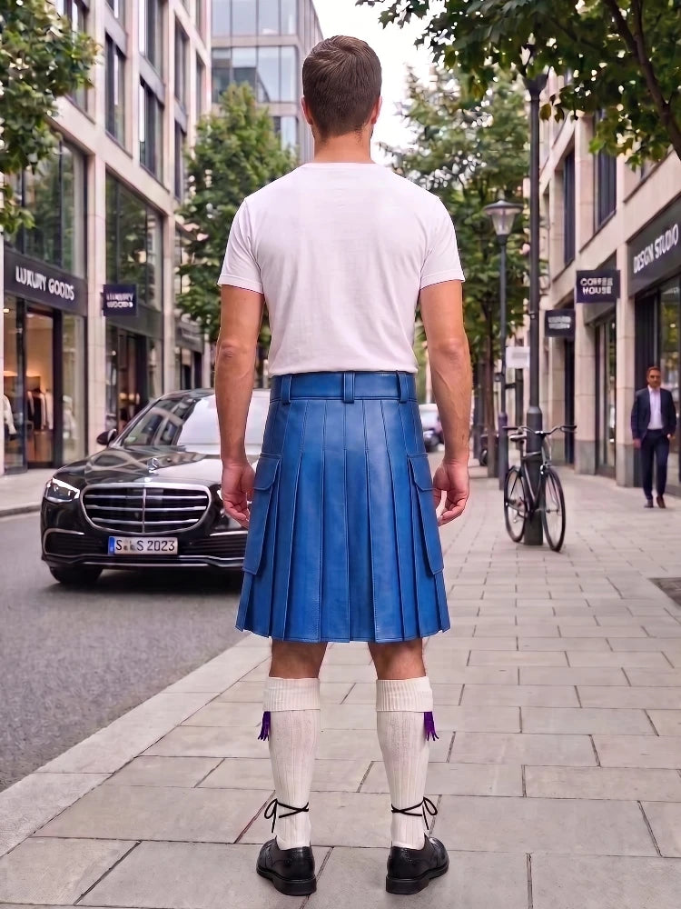 A man viewed from behind wearing a blue leather kilt, white t-shirt, white knee-high socks, and black shoes, standing on a city sidewalk.