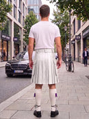 A man viewed from behind wearing a white short-sleeve t-shirt and a pleated white kilt, standing on a city sidewalk with buildings, cars, and a bicycle in the background.